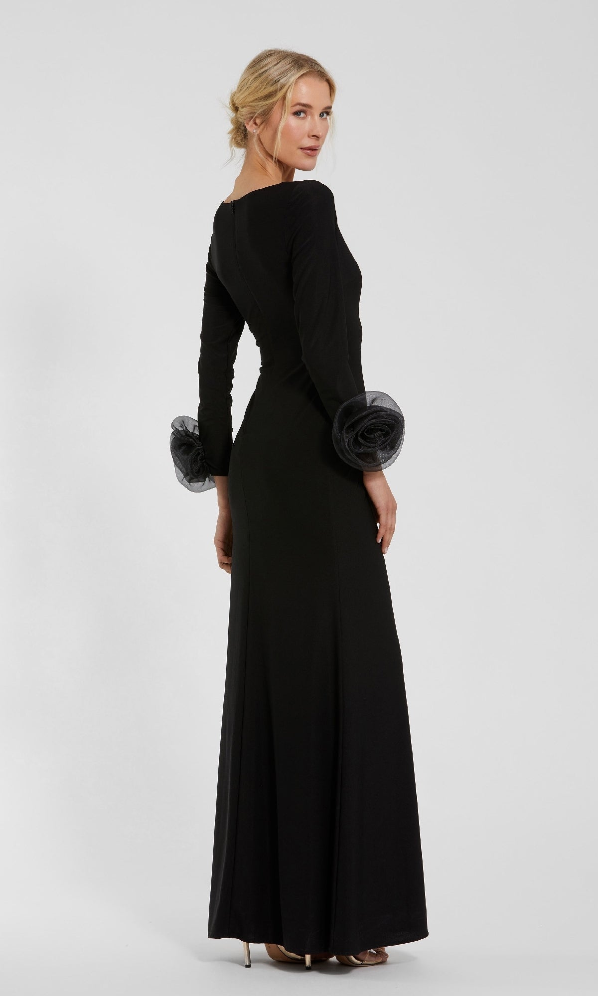 A woman wears the Mac Duggal 49949 Long Sleeve Long Formal Dress, posing back to the camera and turning her head, set against a plain light background.